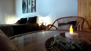 A cozy room with a wooden ceiling, a bed with dark bedding, a chair with a patterned cushion, and a table with a candle. - Your Nomadic Room: Africa (MARTHOD)