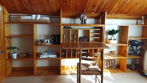 A wooden room with a central table and chairs, surrounded by shelves with various items. - Your Nomadic Room: Africa (MARTHOD)