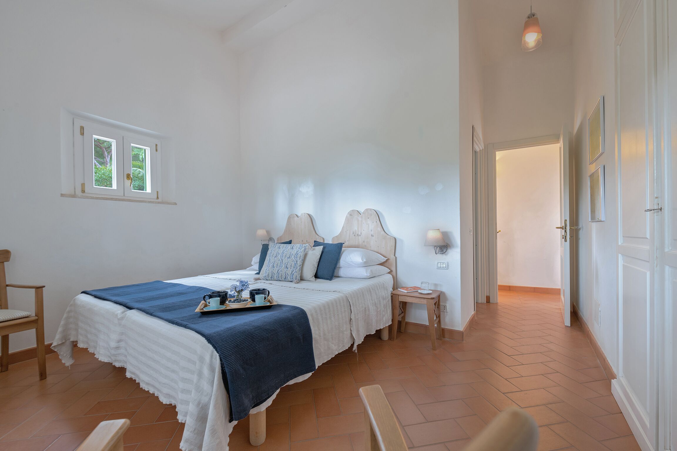 A bedroom with a bed, bedside tables, a window, and a door.