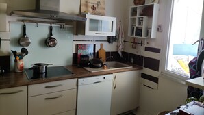 Ett kompakt kök med vita skåp, en diskmaskin från Bosch, upphängda kastruller och ett fönster med utsikt.