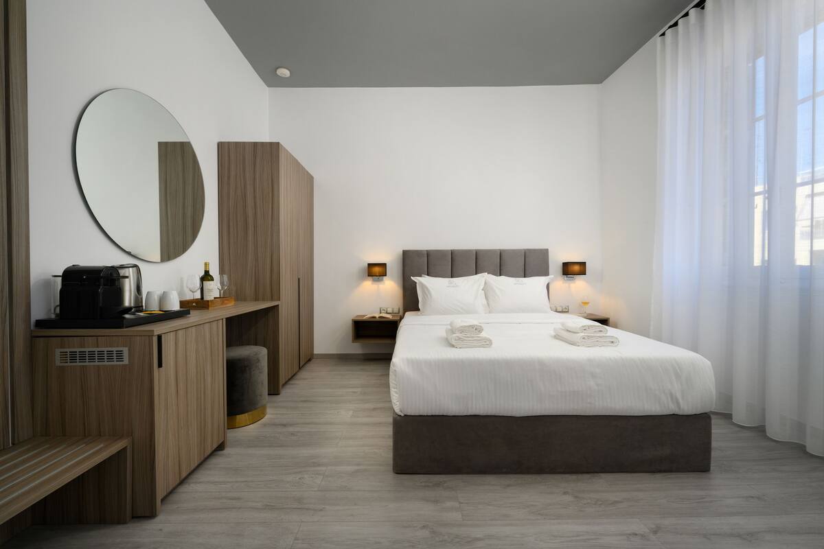 Une chambre d’hôtel moderne avec un grand lit, une table de chevet avec une lampe, un miroir et un banc en bois.