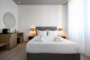Una habitación de hotel moderna con una cama grande, dos mesitas de noche con lámparas, un escritorio de madera, un espejo redondo y una pequeña zona de estar.