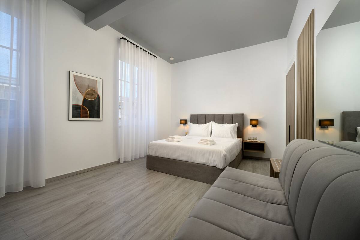 Une chambre d’hôtel moderne avec un grand lit, un canapé et une grande fenêtre avec des rideaux.
