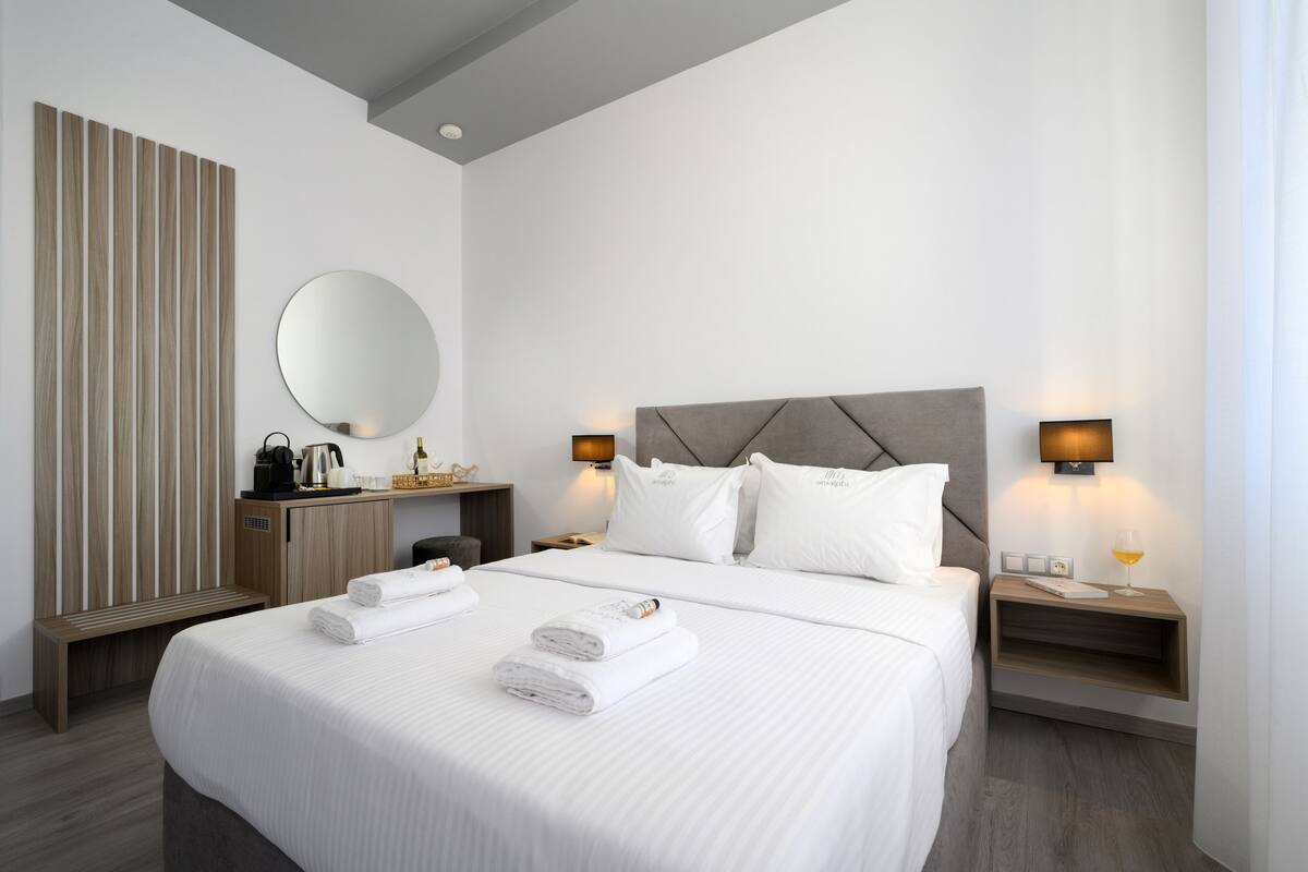 Une chambre d’hôtel moderne avec un grand lit, un banc en bois, un miroir rond et deux tables de chevet avec des lampes.