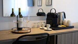 Una habitación de hotel con un escritorio de madera, dos botellas de vino, copas de vino, una cafetera, un hervidor y una bandeja con tazas y platos.