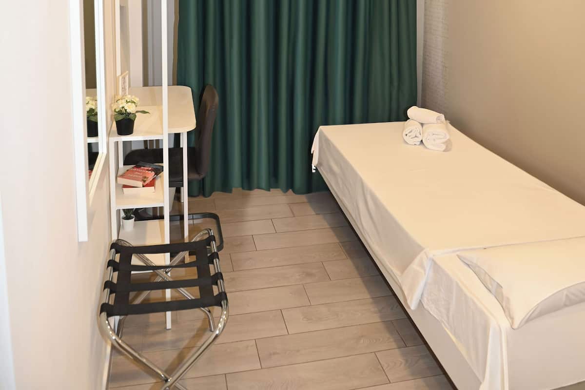 A small, neatly arranged room with a bed, a chair, a table with a plant, and a mirror.