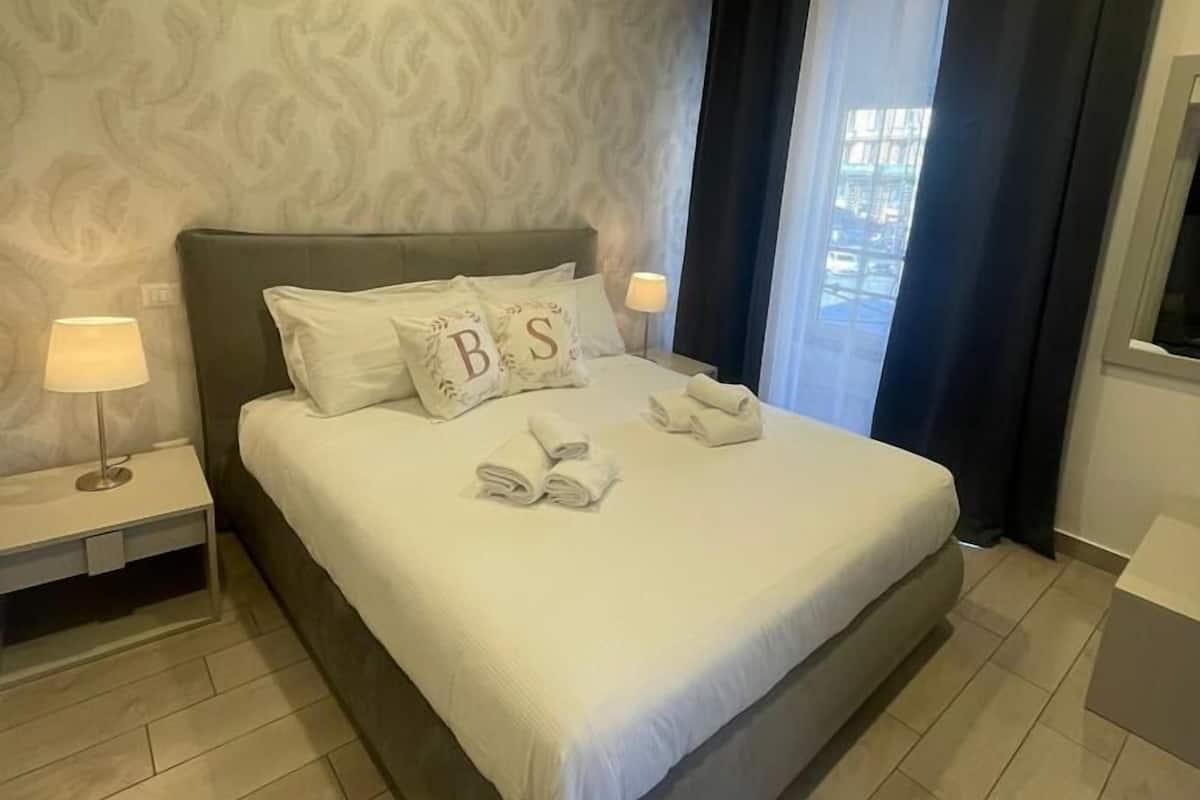 A neatly made bed with pillows, a bedside lamp, and a folded towel on the floor.