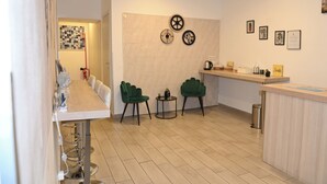 Une cuisine moderne avec un long comptoir, deux chaises vertes, une petite table ronde et des œuvres d’art décoratives accrochées au mur.