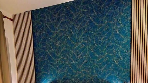 Une chambre d’hôtel comprenant un lit, une tête de lit, deux tables de chevet et un mur orné d’un motif de feuilles.