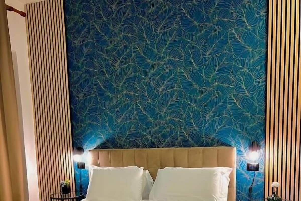 A hotel room with a bed, a headboard, two bedside tables, and a wall with a leaf pattern.