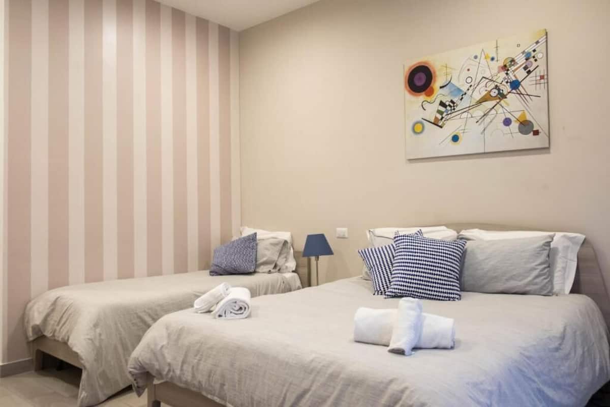 A hotel room with two beds, striped wallpaper, and a modern abstract painting on the wall.