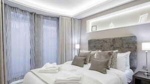 Ein modernes Hotelzimmer mit einem großen Bett, einem Kopfteil mit steinartiger Struktur und einem Fenster mit durchsichtigen Vorhängen.