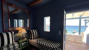 A room with a checkered bed, striped pillows, a mirror, a lamp, and a view of the sea through a window.