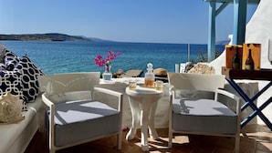 A terrace with two white chairs, a small table, and a view of the sea.