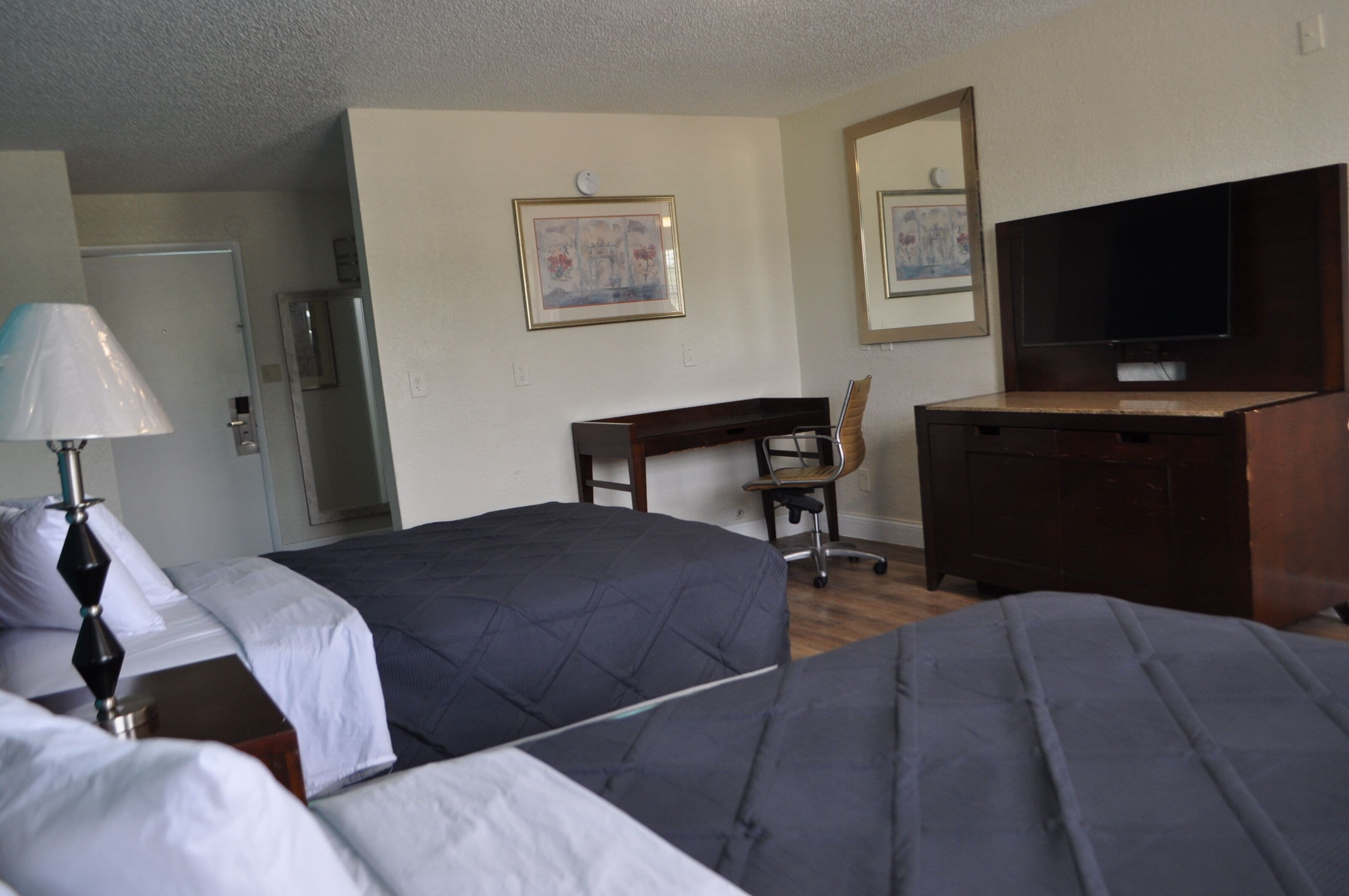 A hotel room with two beds, a desk, a chair, a television, and a refrigerator.