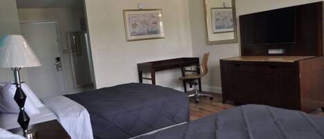 A hotel room with two beds, a desk, a chair, a television, and a refrigerator.