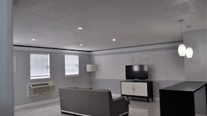 A modern living room with a grey sofa, a black entertainment unit, and a white cabinet. - Apm Inn and Suite  (Jacksonville)
