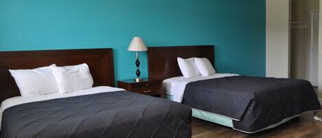 Habitación de hotel con dos camas, paredes verde azulado, cabeceros de madera y una mesita de noche con lámpara.