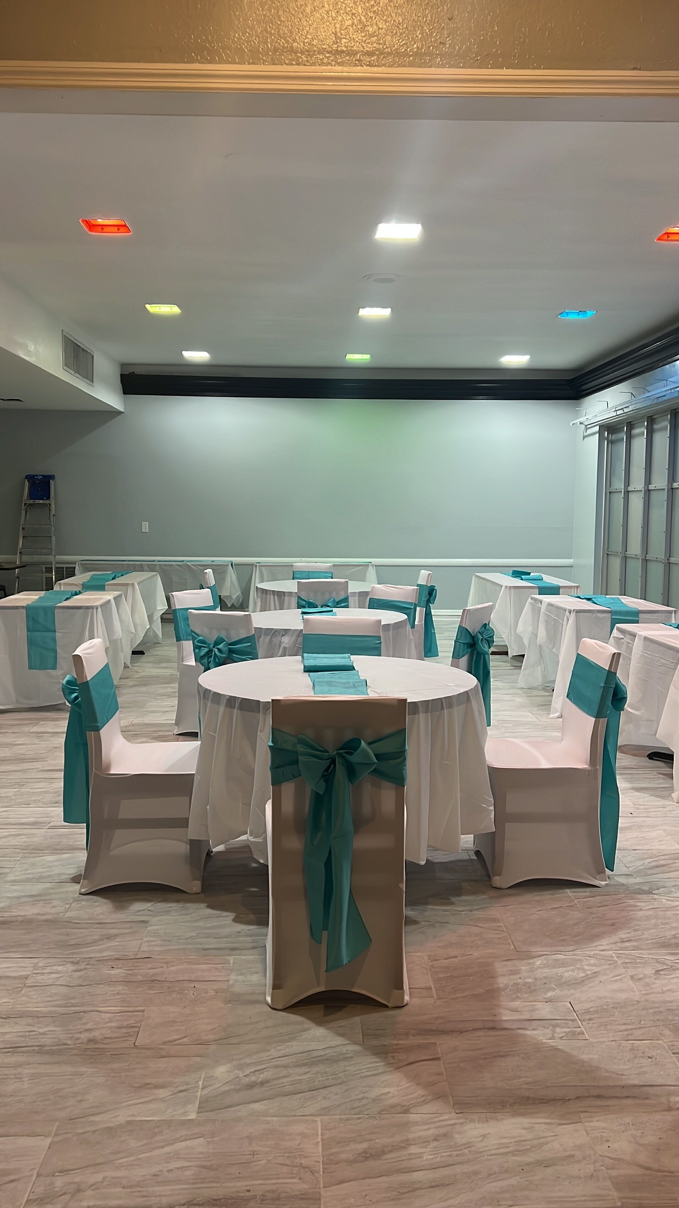 A conference room with round tables, chairs with teal sashes, and a white ceiling with recessed lighting.