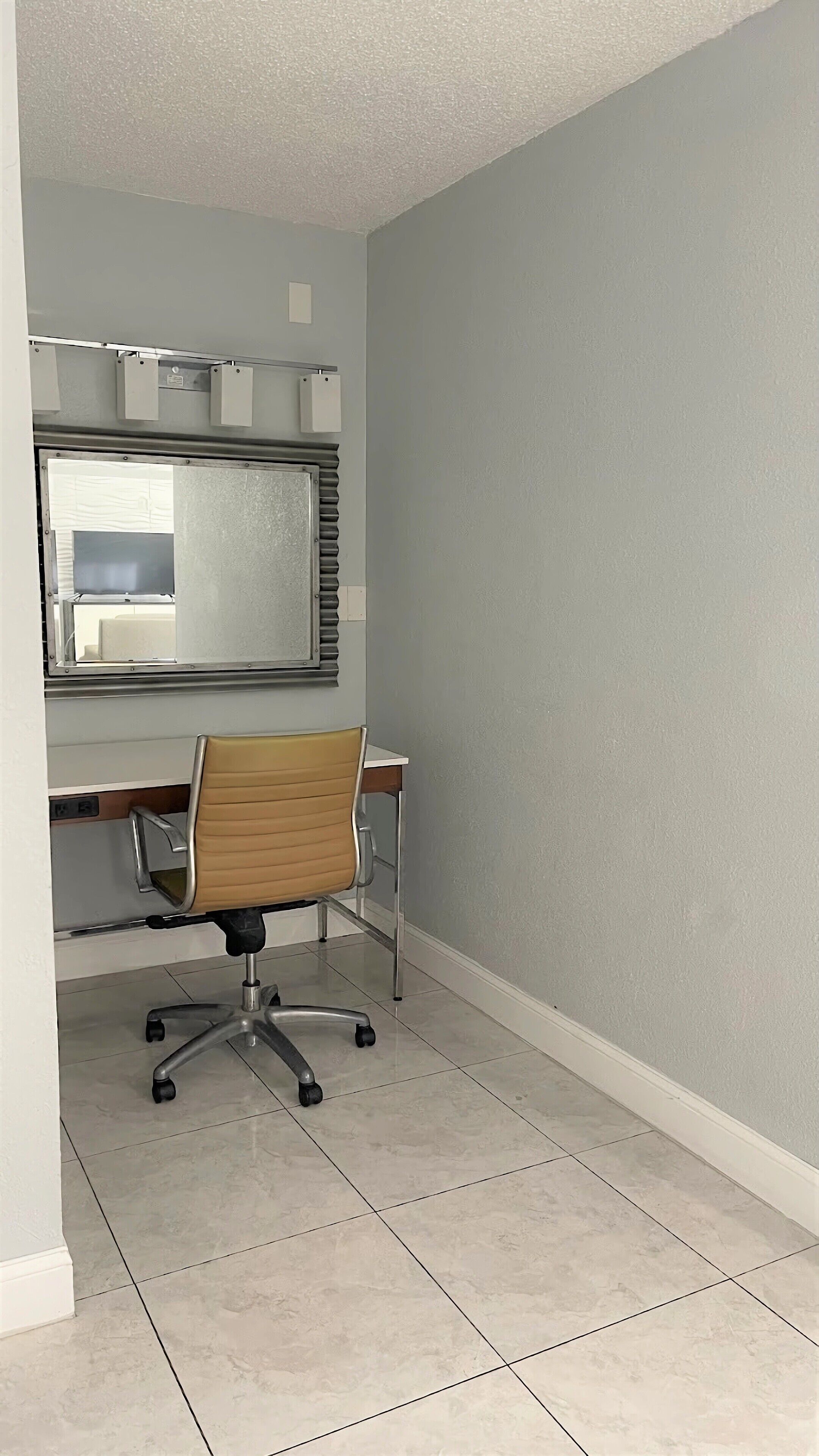 Ein kleiner Arbeitsraum mit Schreibtisch, Stuhl und einem großen Spiegel an der Wand.