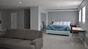 A modern hotel room with a large bed, a sofa, a desk, and a window. - Apm Inn and Suite  (Jacksonville)