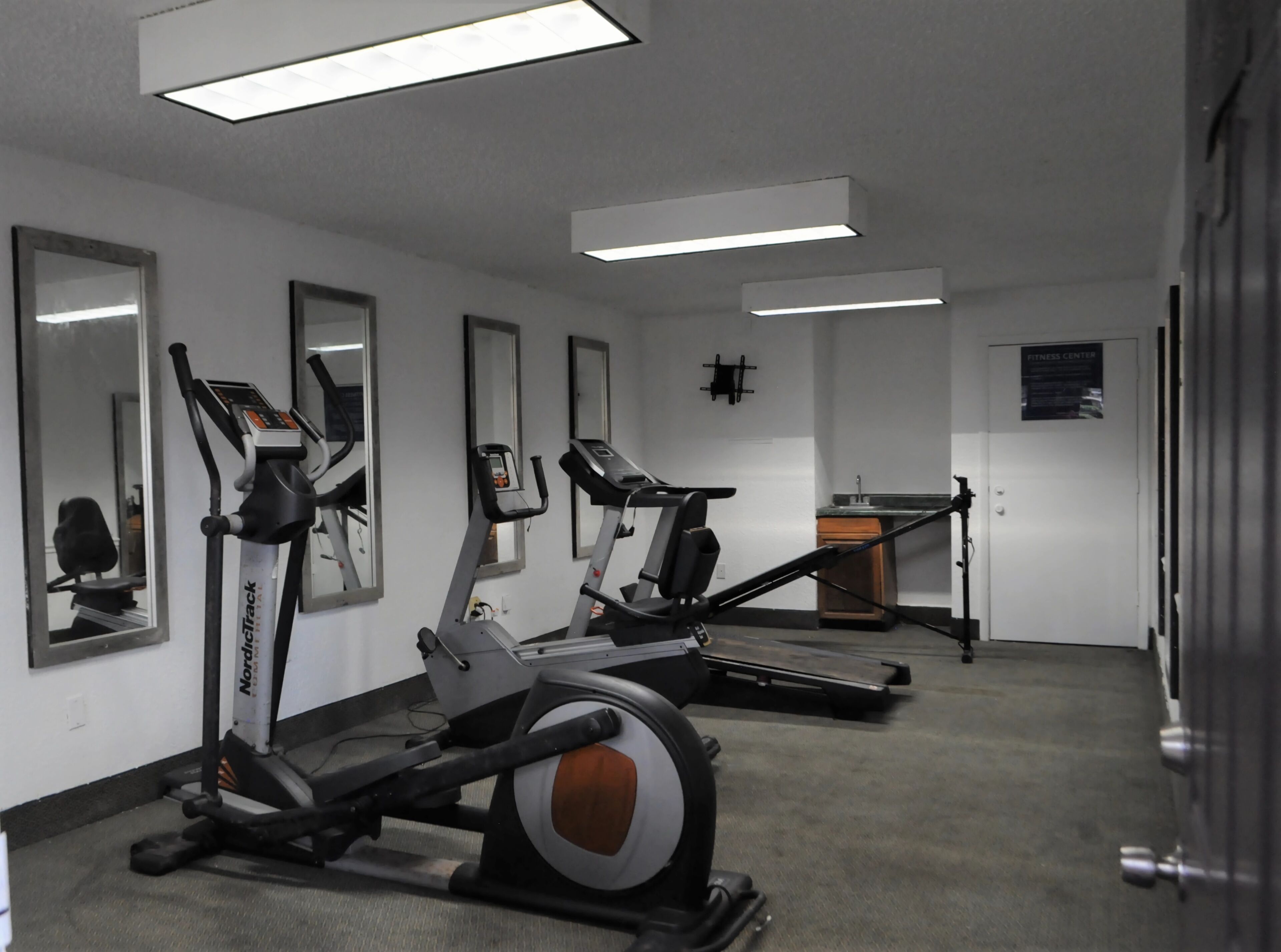 Une salle de sport équipée de tapis de course, de vélos d’appartement et d’un mur entièrement recouvert de miroirs.
