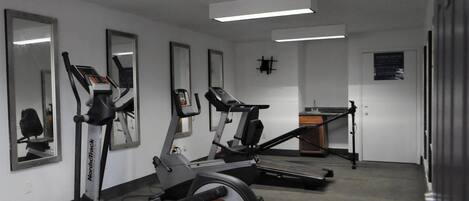 Une salle de sport équipée de tapis de course, de vélos d’appartement et d’un mur entièrement recouvert de miroirs.