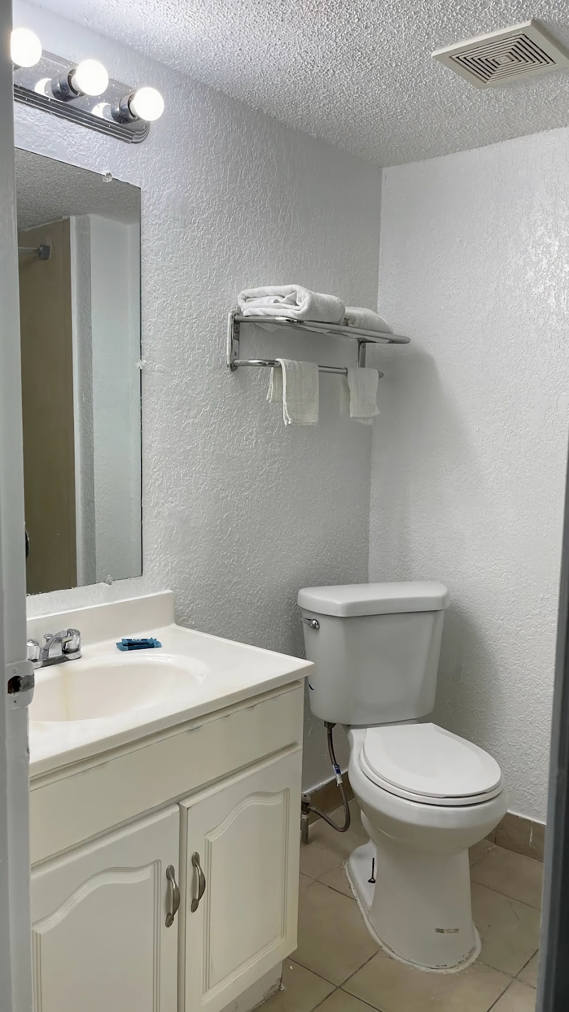 Un baño con un lavamanos blanco, un inodoro y un espejo con luces arriba.
