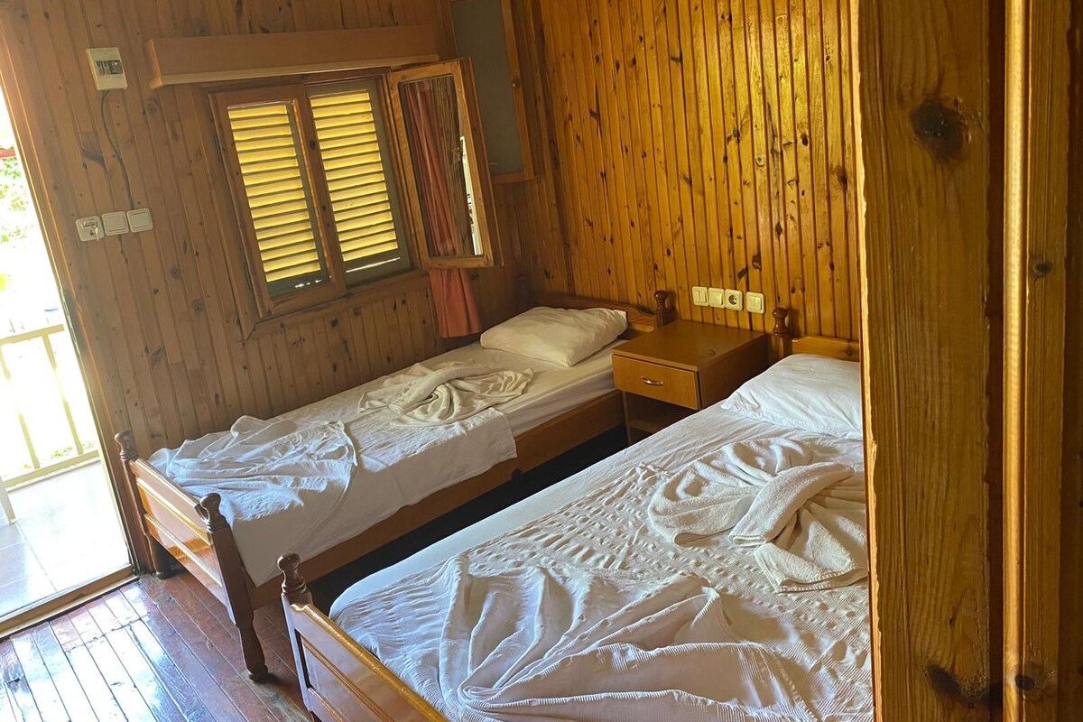 A wooden cabin bedroom with two single beds, a small wooden nightstand, and a window with shutters.