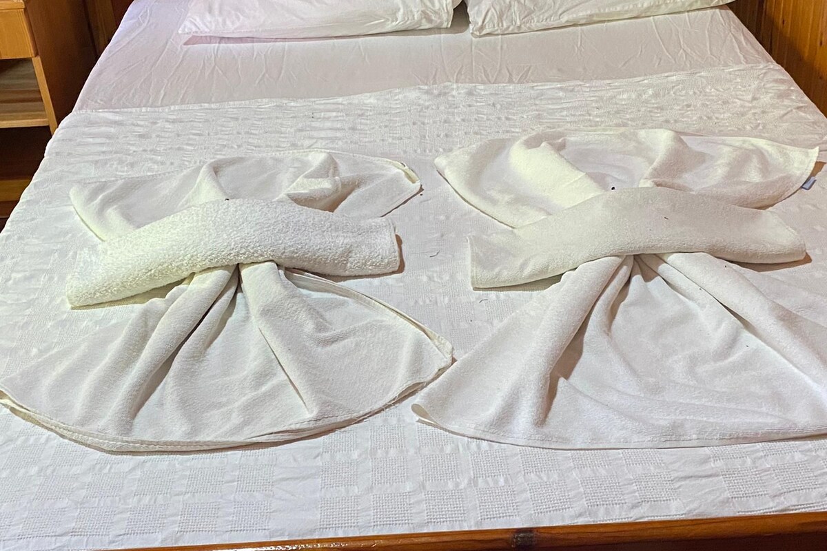 A bed with white linens and two towels folded on top.