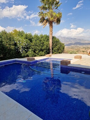 A swimming pool with blue tiles, surrounded by greenery and a view of mountains. - Lovely family villa overlooking Lake and Mountains 15 mins from Coast (Viñuela)