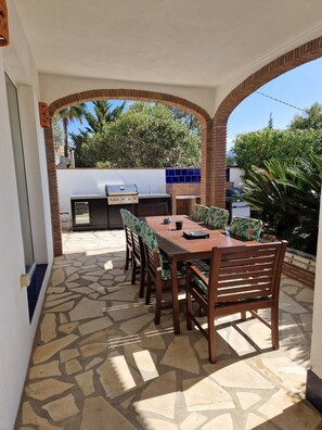 An outdoor patio with a wooden table and chairs, a barbecue grill, and a patterned tablecloth. - Lovely family villa overlooking Lake and Mountains 15 mins from Coast (Viñuela)