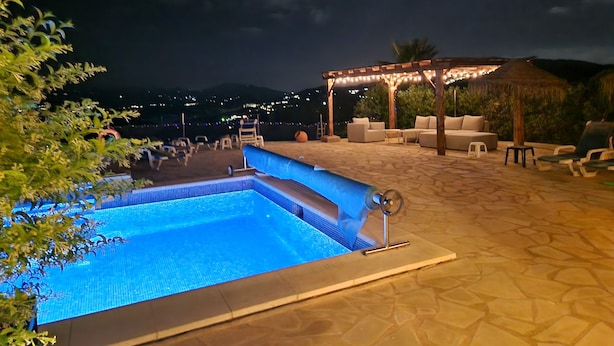 A swimming pool with a pergola and lounge chairs in the background.