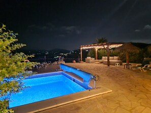 Una piscina con una pérgola y sillones de descanso al fondo.