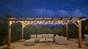An outdoor patio with stone flooring, a wooden pergola, string lights, and a beige sofa set.