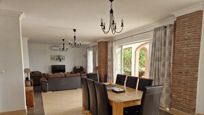 A dining area with a wooden table and chairs, a TV in the background, and a brick wall.