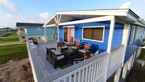 A blue mobile home with a covered porch, outdoor seating, and a red door.