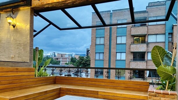 Una terraza en la azotea con un brasero, asientos de madera y vistas a la ciudad.