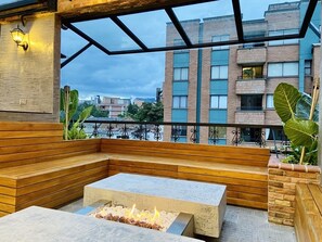 A rooftop terrace with a fire pit, wooden seating, and a view of the cityscape. - Casa Santafe - Coliving Hotel (Medellín)