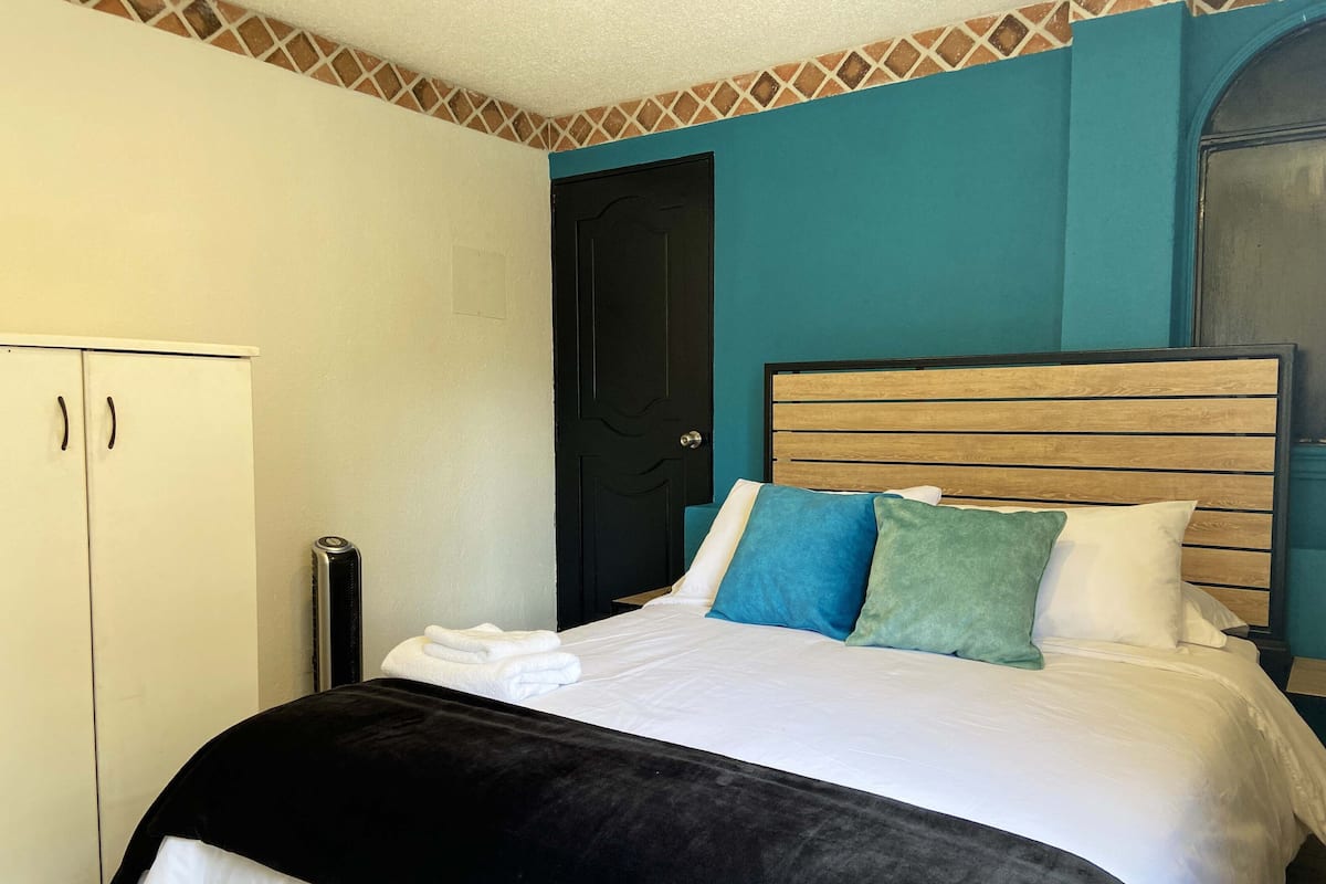 A bedroom with a bed, a black radiator, a white wardrobe, and a black door.