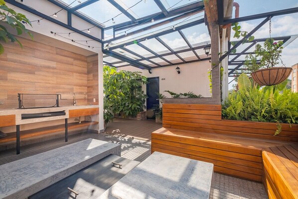 Un espace cuisine extérieur moderne, doté d’un banc en bois, d’un évier encastré et d’un pot à suspendre pour les plantes.