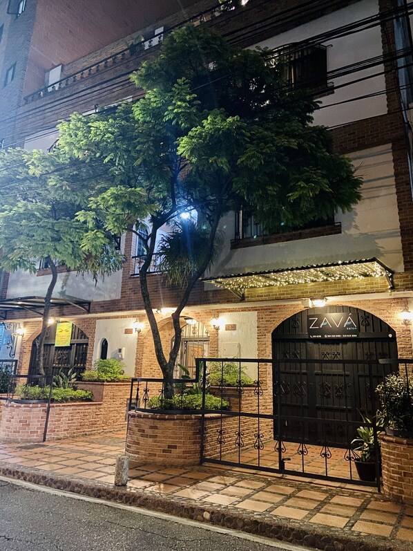 A brick building with a gated entrance, a tree in front, and a sign for 'ZAVA salon'. - Casa Santafe - Coliving Hotel (Medellín)