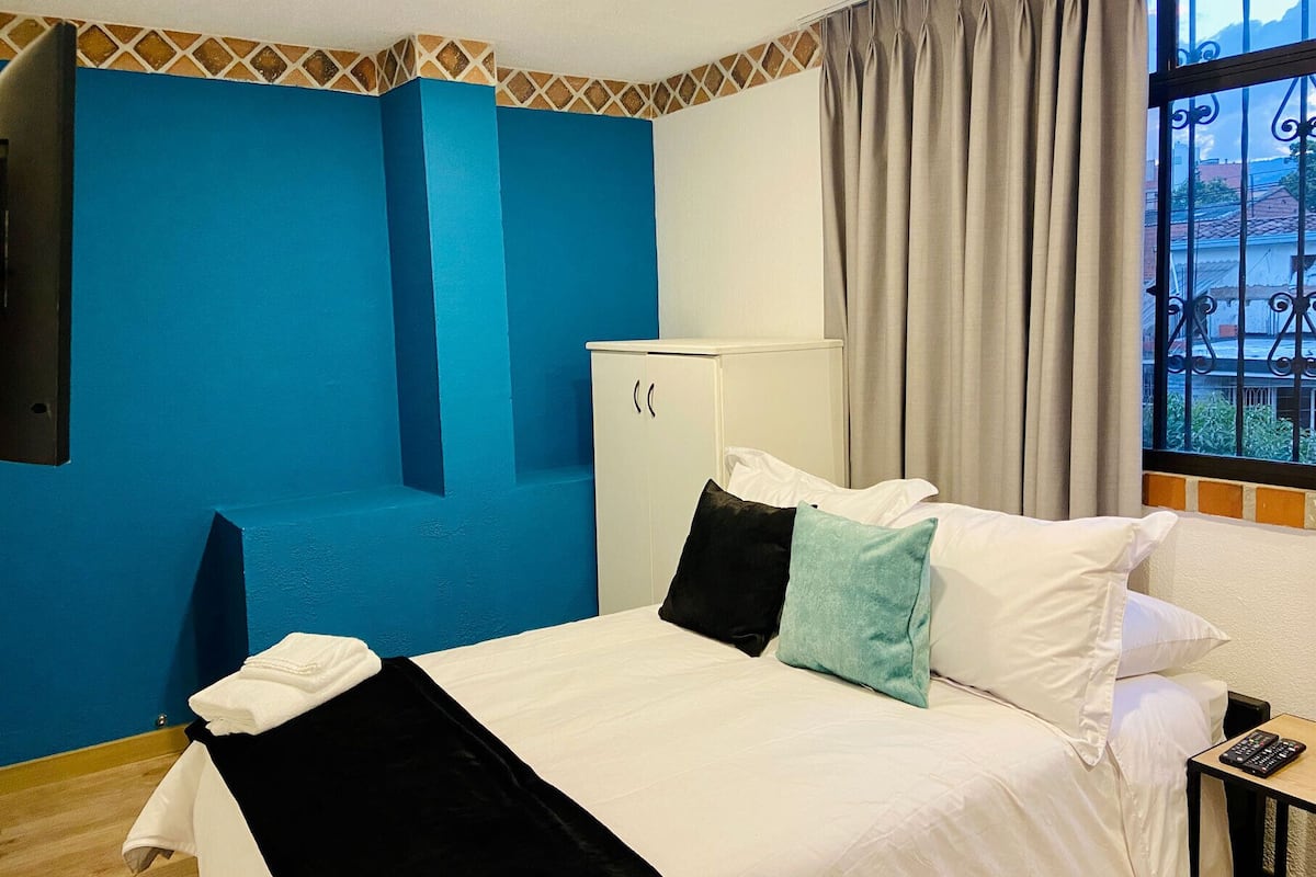 A hotel room with a bed, a desk, a wardrobe, and a window with curtains.