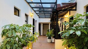Un pasillo exterior cubierto con paredes de ladrillo, plantas en macetas y suelo de baldosas.