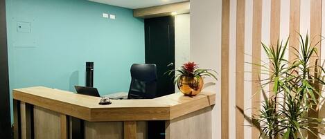 A reception desk with a laptop, a chair, and a potted plant.