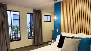 Un dormitorio moderno con una cama grande, dos ventanas con cortinas, una pared de acento de madera y una lámpara colgante.