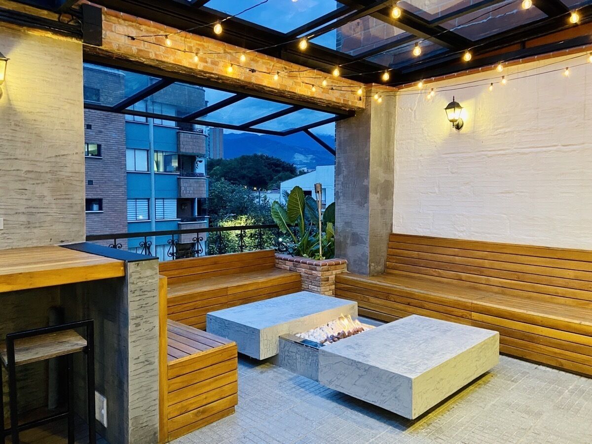 Un espace extérieur aménagé avec des bancs en bois et un foyer, le tout sous une verrière illuminée de guirlandes lumineuses.