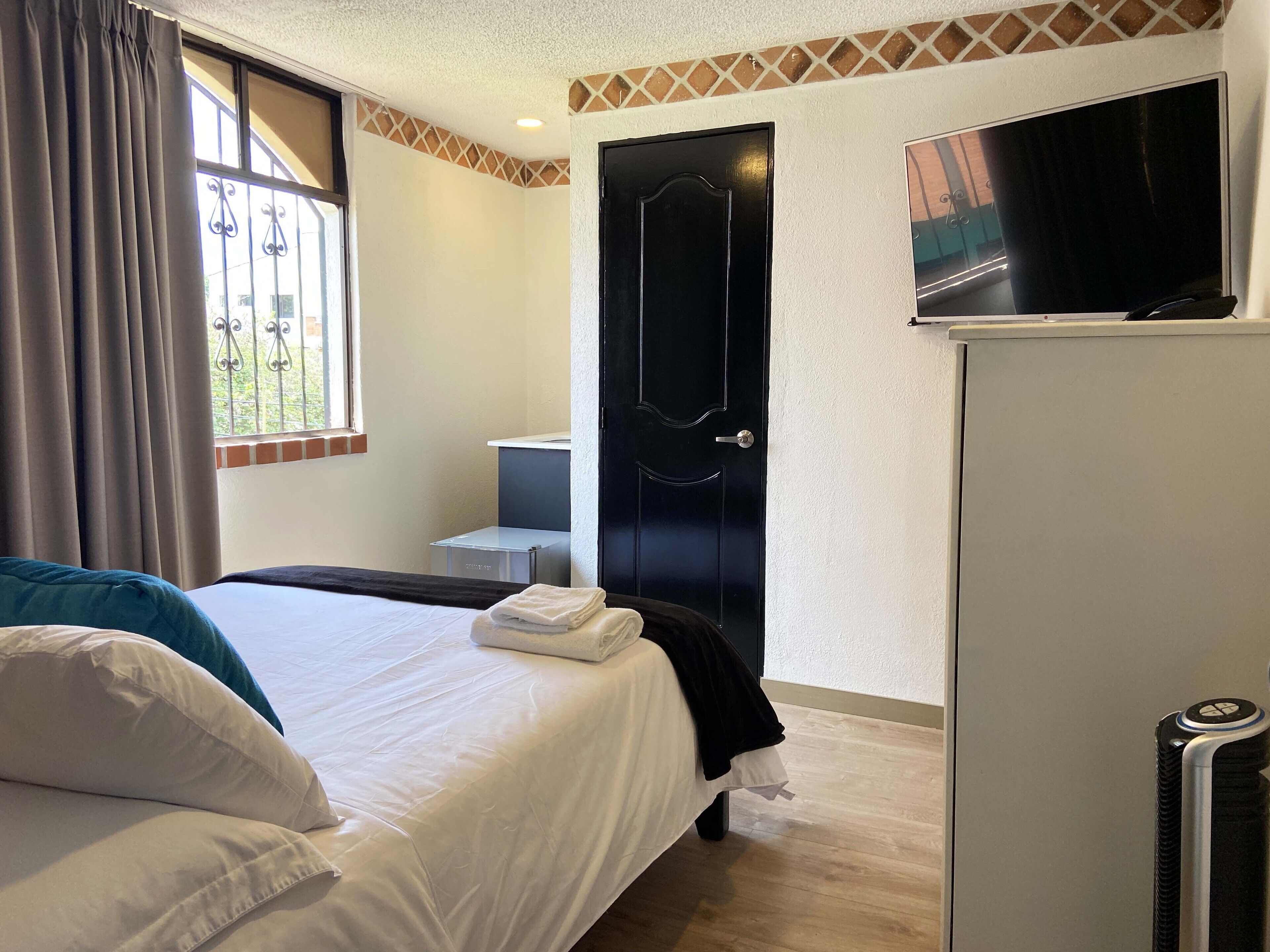 Habitación de hotel con cama, televisión, armario y ventana con cortinas.