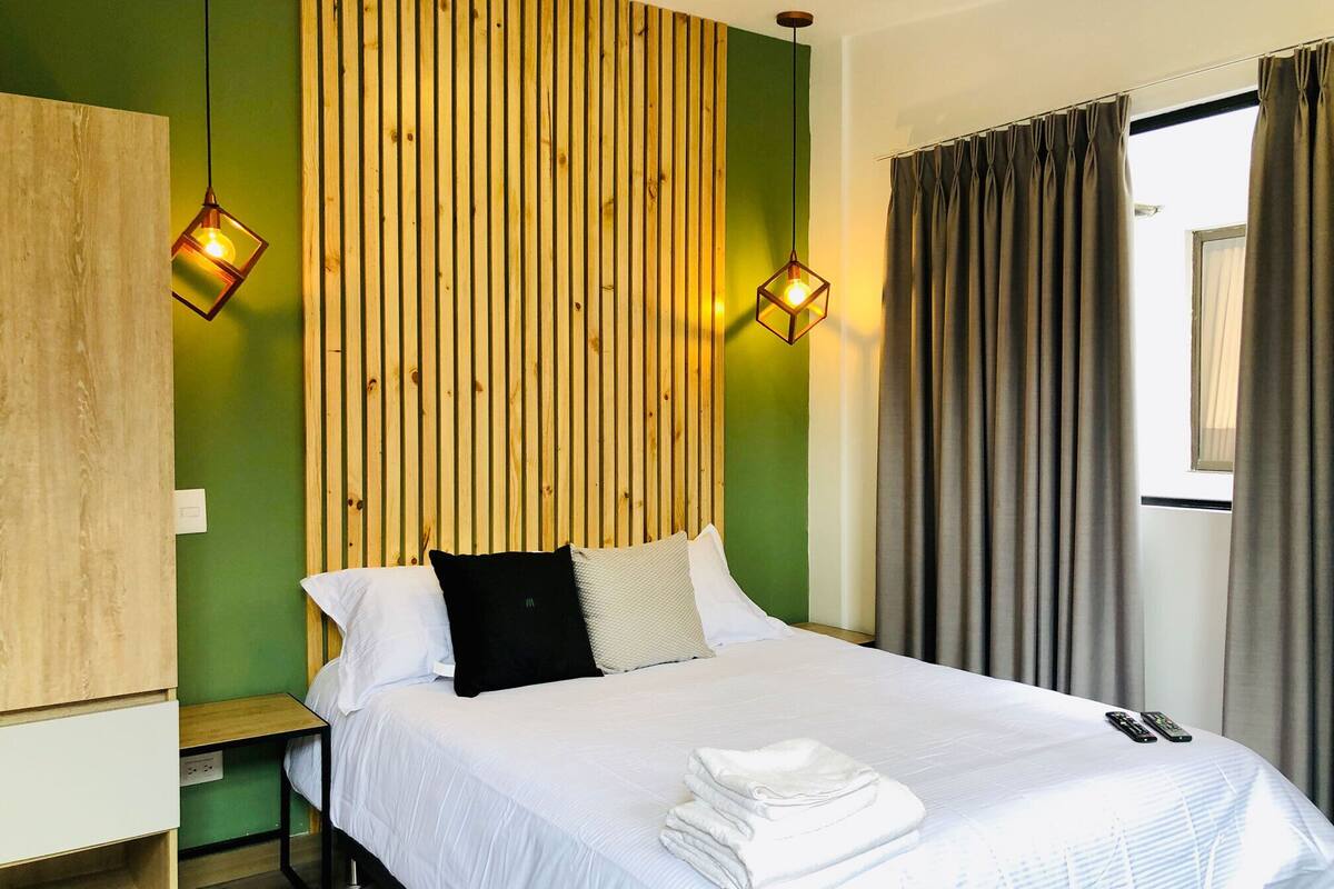 A hotel room with a bed, a wooden slat wall, a nightstand, and a window with curtains.