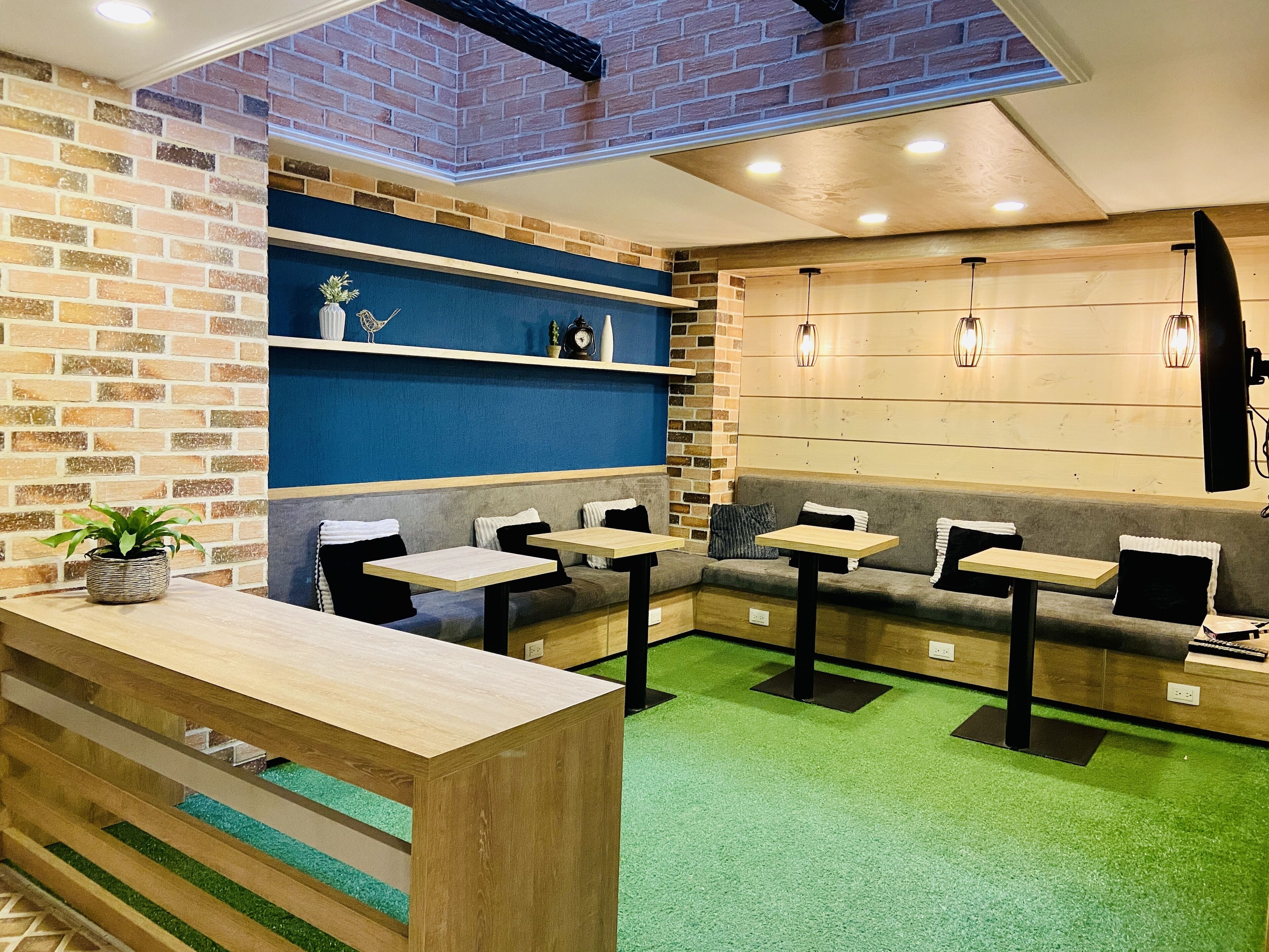 A restaurant with brick walls, blue and wooden accents, green carpet, and multiple seating areas including tables and benches.